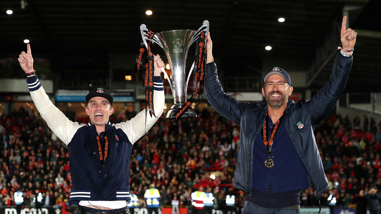 Rob McElhenney and Ryan Reynolds holding the Vanarama National League football trophy